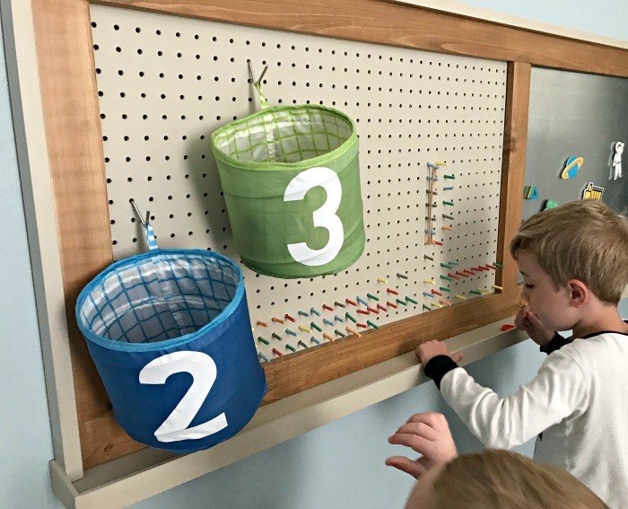 A pegboard with colorful pegs to make designs and bins for basketball hoops. Build a fun DIY Modern Farmhouse Kids Activity Wall Board. With 20 Ideas for board options that work for kids, teens, and adults. #ModernFarmhouse #KidsFurniture #DIYKids #AbbottsAtHome