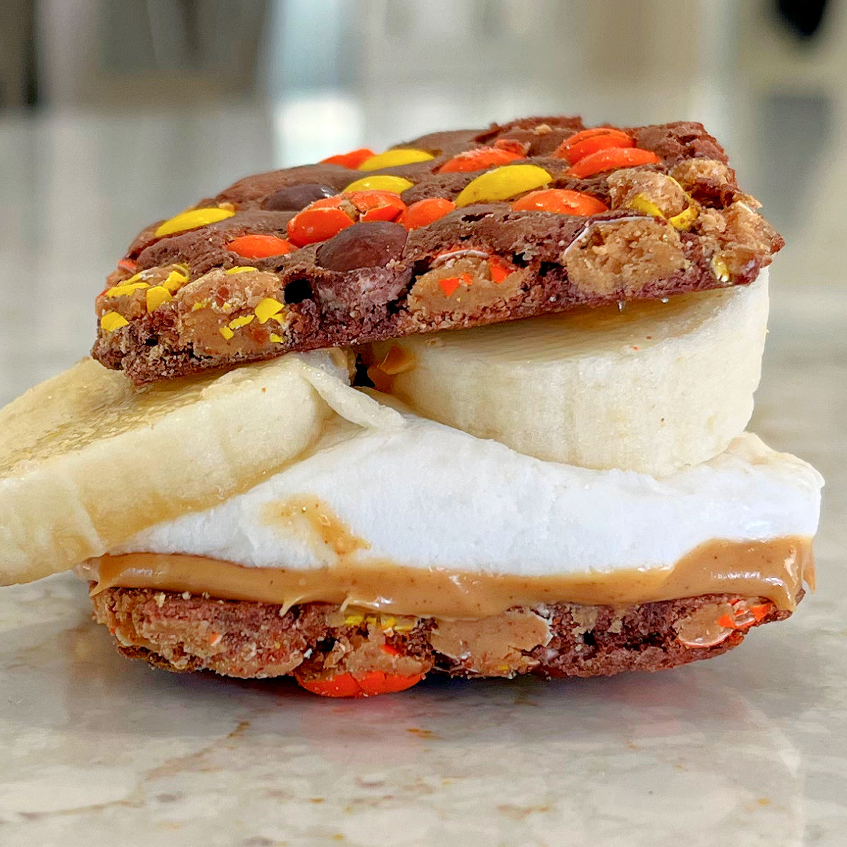 One example of 15 ways to make Smore's with Peanut Butter at home. Image shows Reese's Pieces Brownie Brittle, banana, marshmallow and peanut butter Smores.